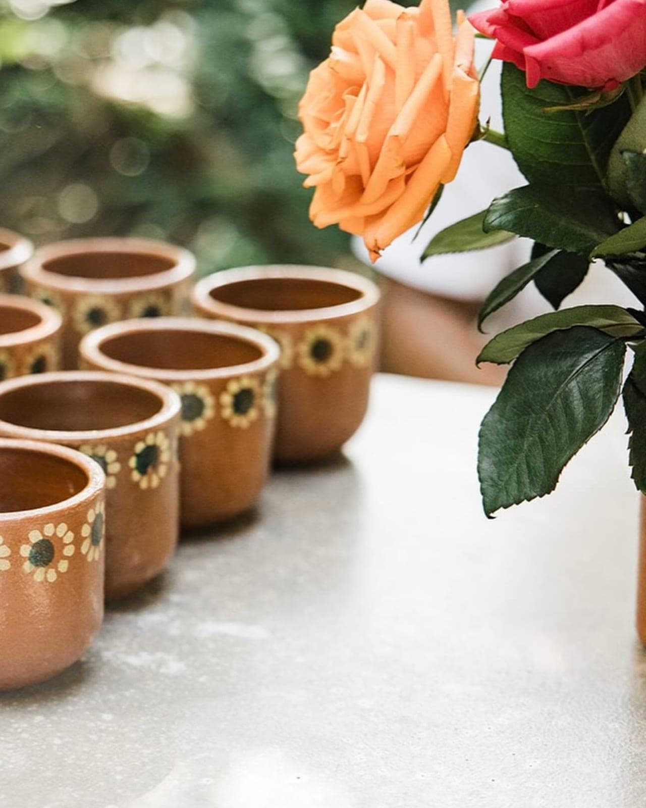 Rows of floral-painted terracotta ceremony cups beside roses, jungle light behind