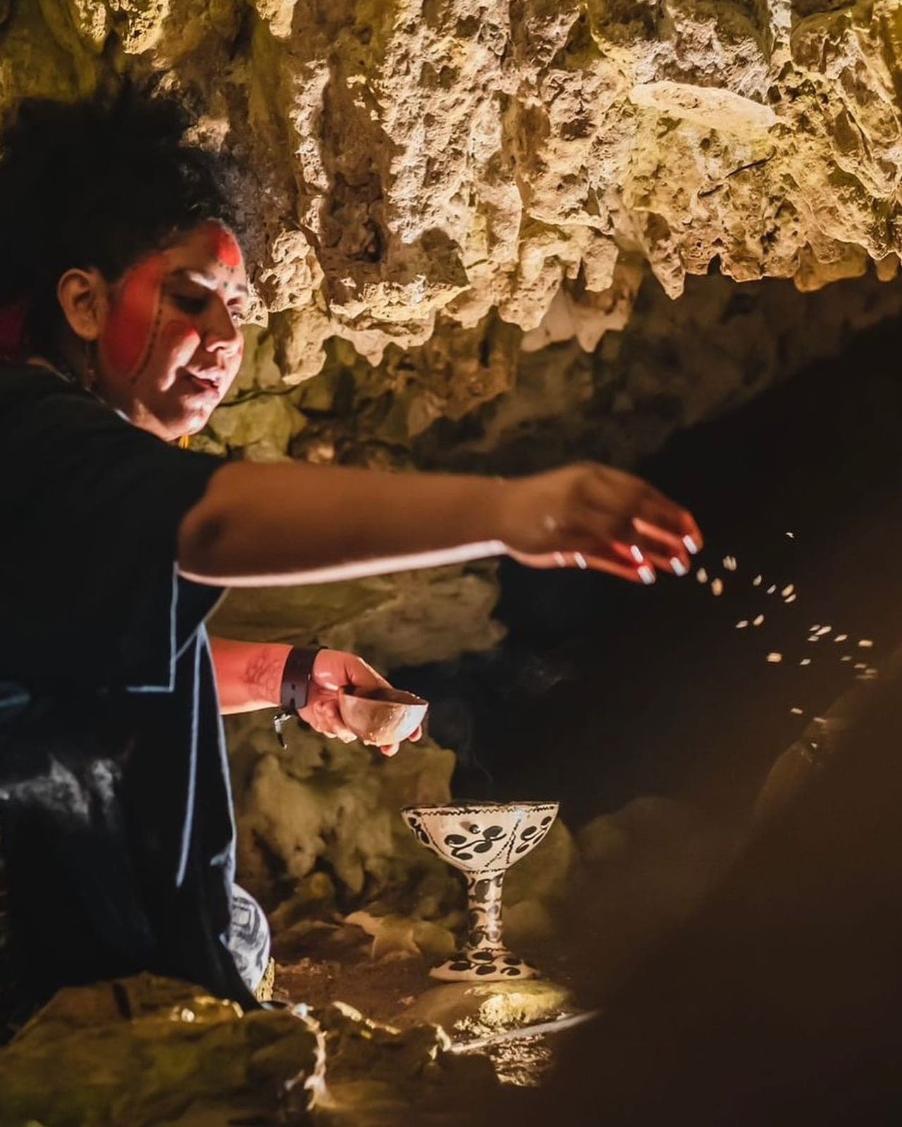 The red-painted ceremonialist sprinkling offerings over a Mayan chalice in the dark cave