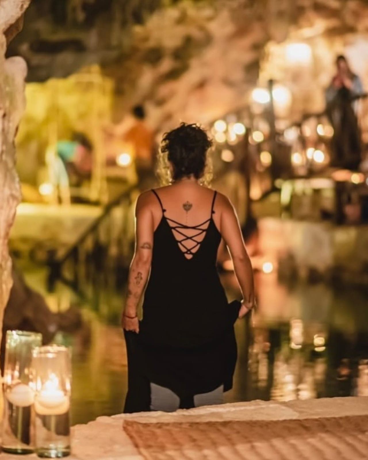 A guest in black walking toward the candlelit water inside the glowing night cave