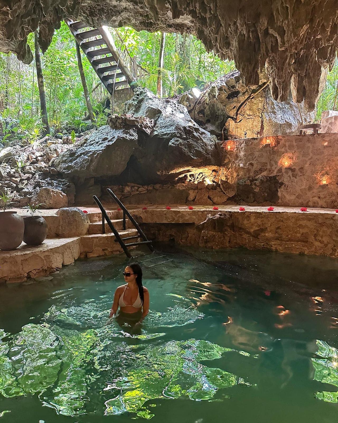 A guest bathing waist-deep in the turquoise cenote, candles and blossoms dressing the stone ledge