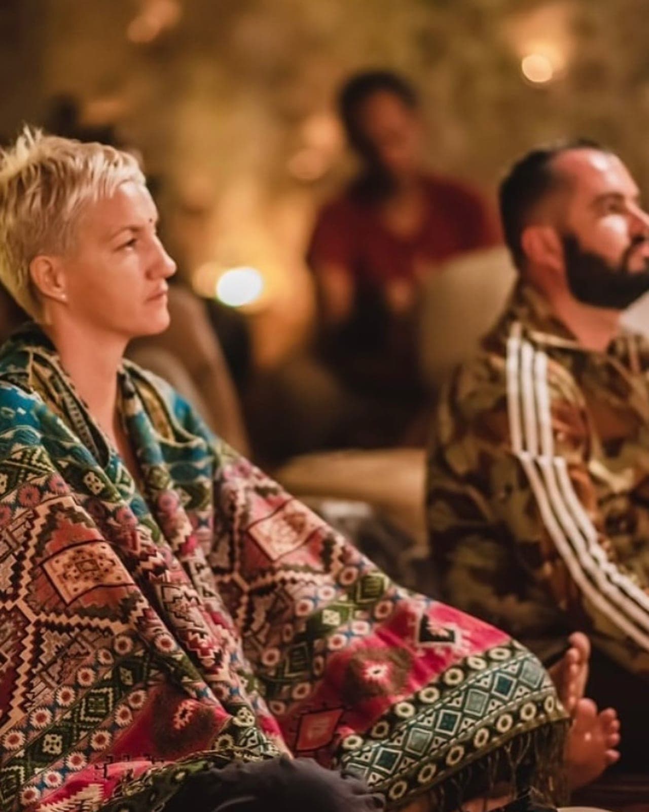 Two guests wrapped in blankets, eyes closed, in the warm light of the cave
