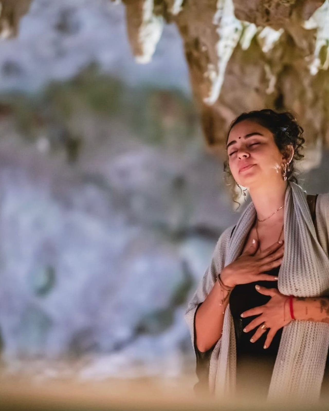 A guest standing with both hands over her heart, the cave wall behind her