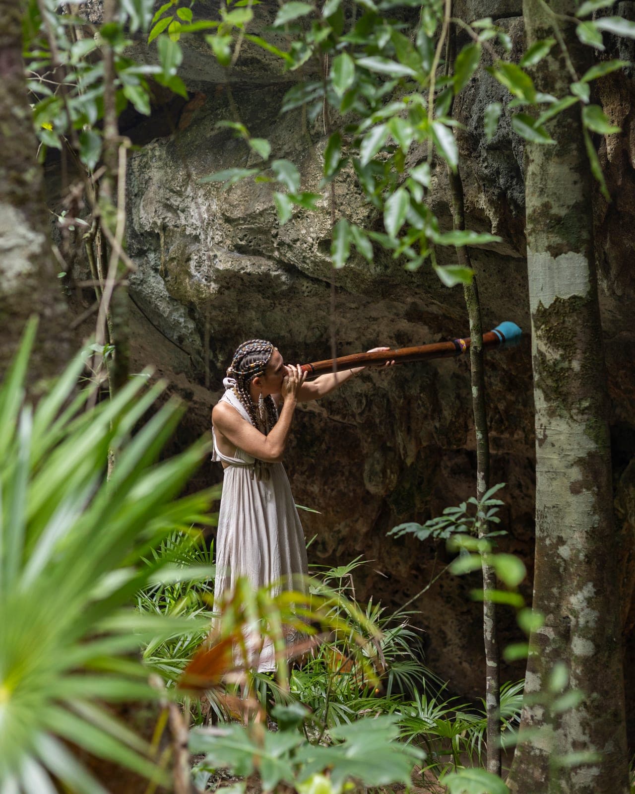 A woman playing a didgeridoo among the jungle greenery