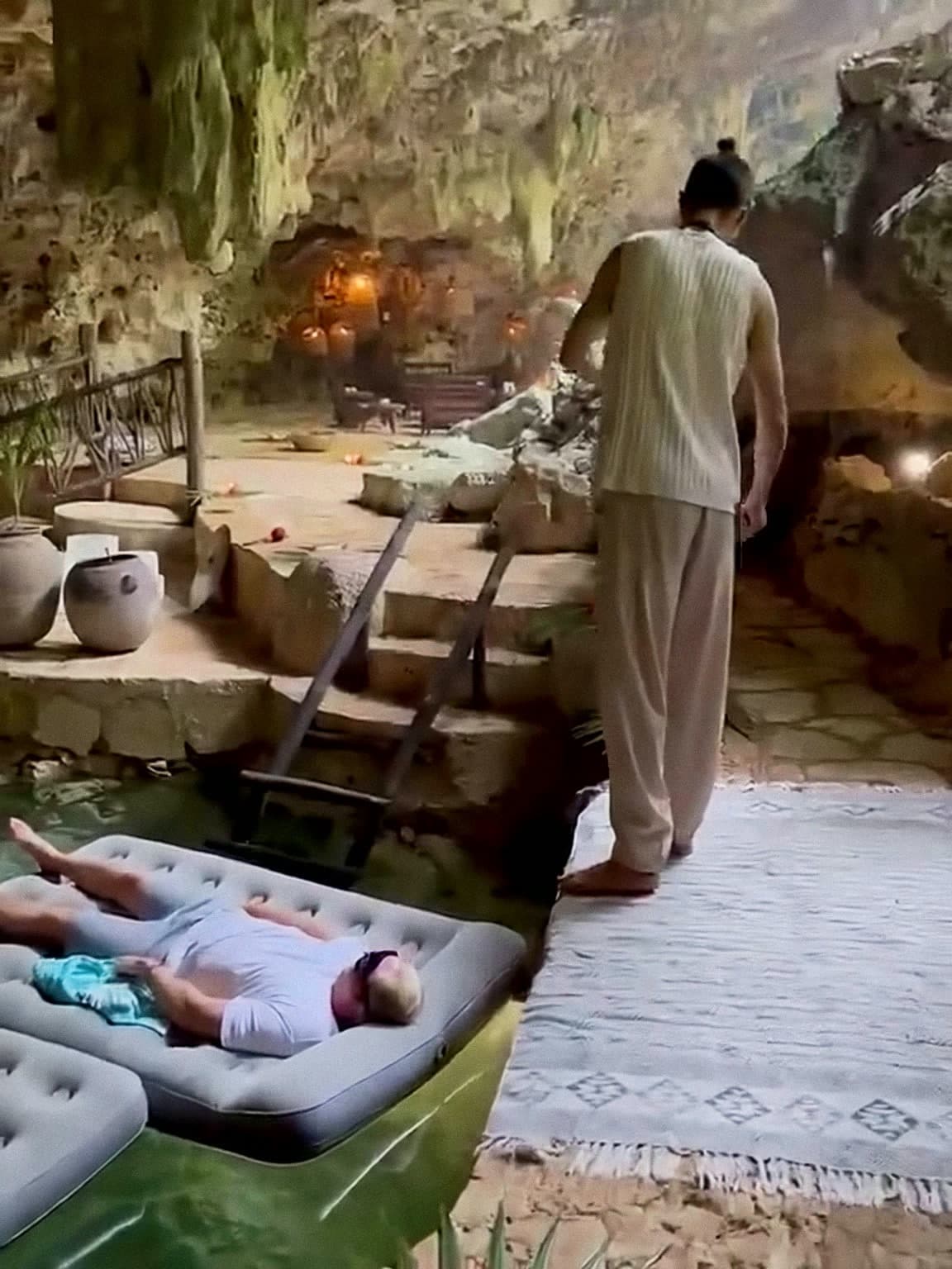 The floating mattress waiting on the still turquoise water of the cenote, candles set along the stone and a plant in a clay urn beside it