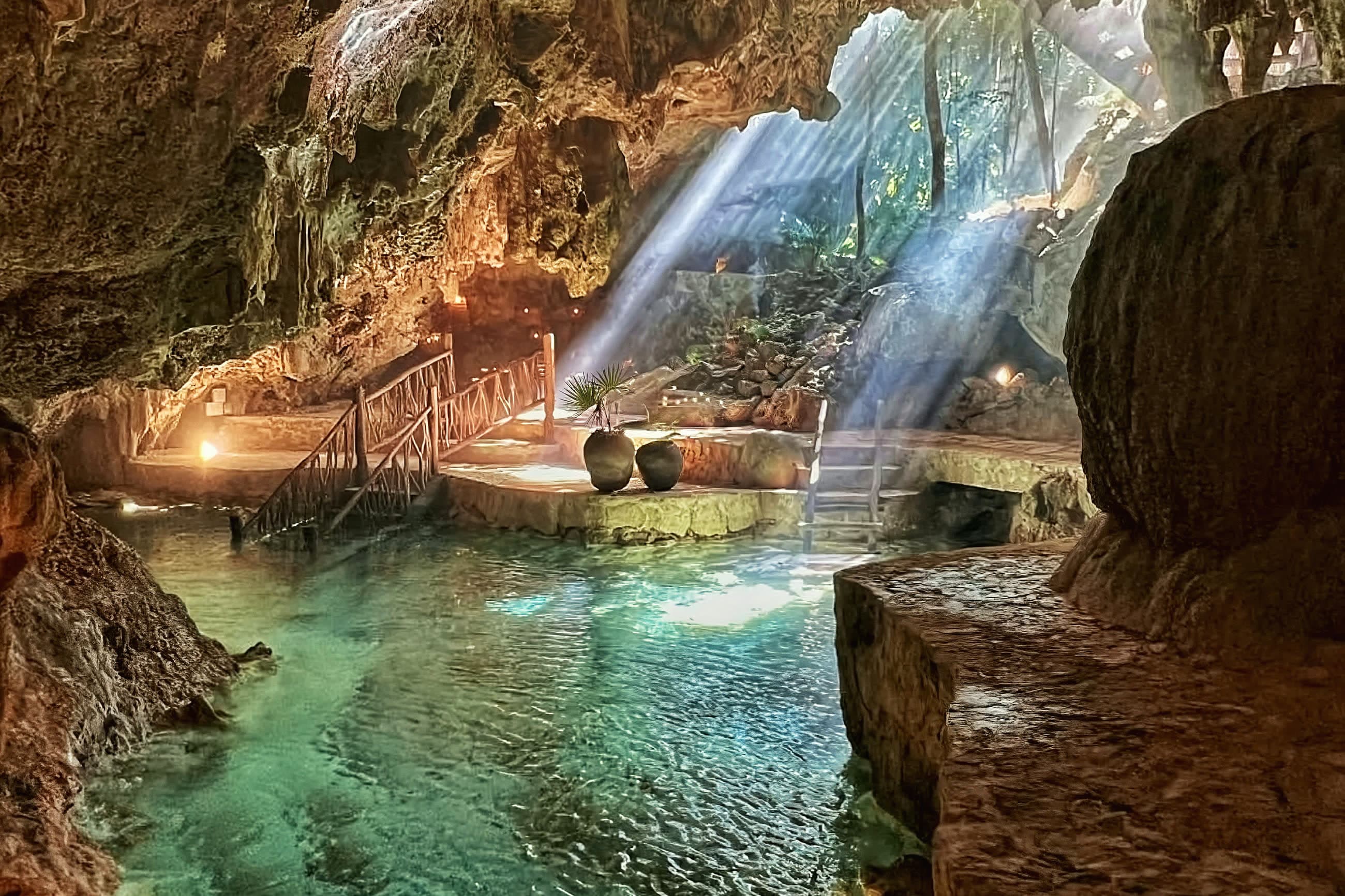 Shafts of morning sun falling through the opening into the cave, the cenote turquoise and clear beneath them