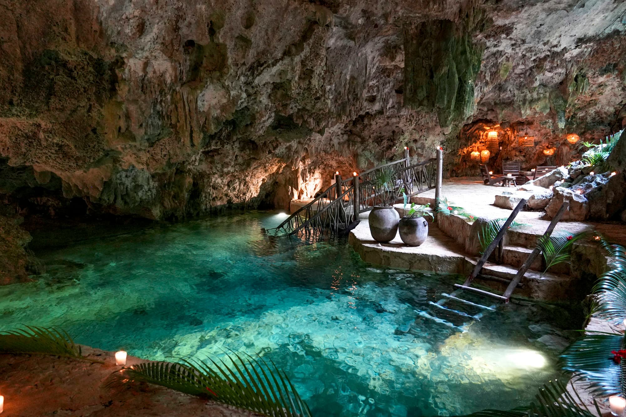 The cenote in daylight: clear turquoise water, the wooden ladder down into it and the clay urns on the stone