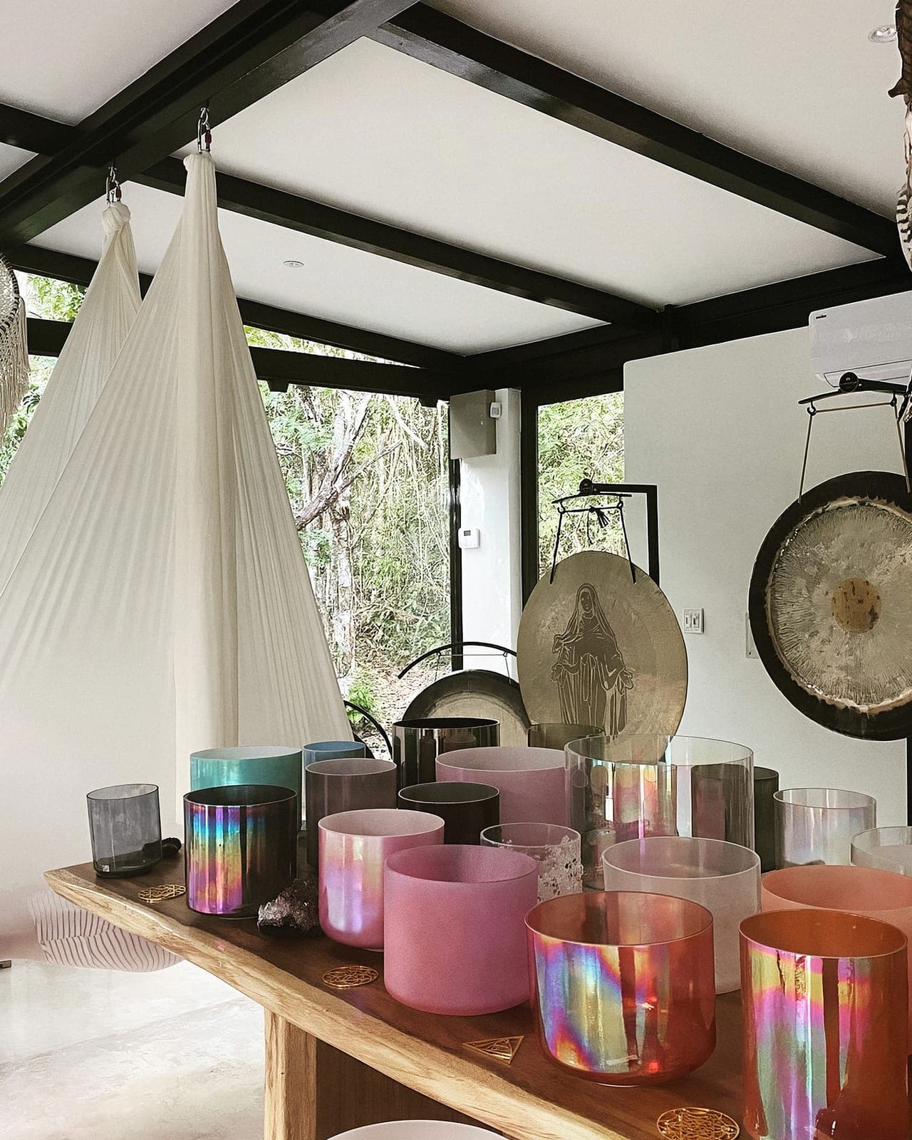The glass Sound Temple dressed for ceremony: silk hammocks, a table of crystal bowls, gongs and dreamcatchers