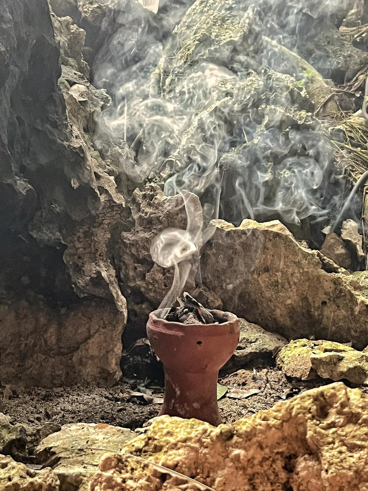 Copal burning in a clay vessel on the limestone at the mouth of the cave, the smoke rising against the rock
