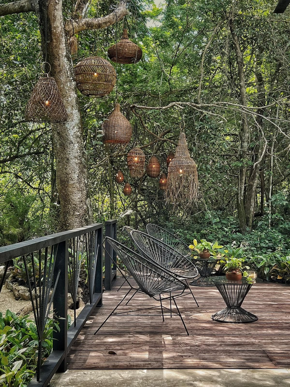 The lounge deck seen from the walkway, woven lanterns of every shape hanging from the branch above the chairs