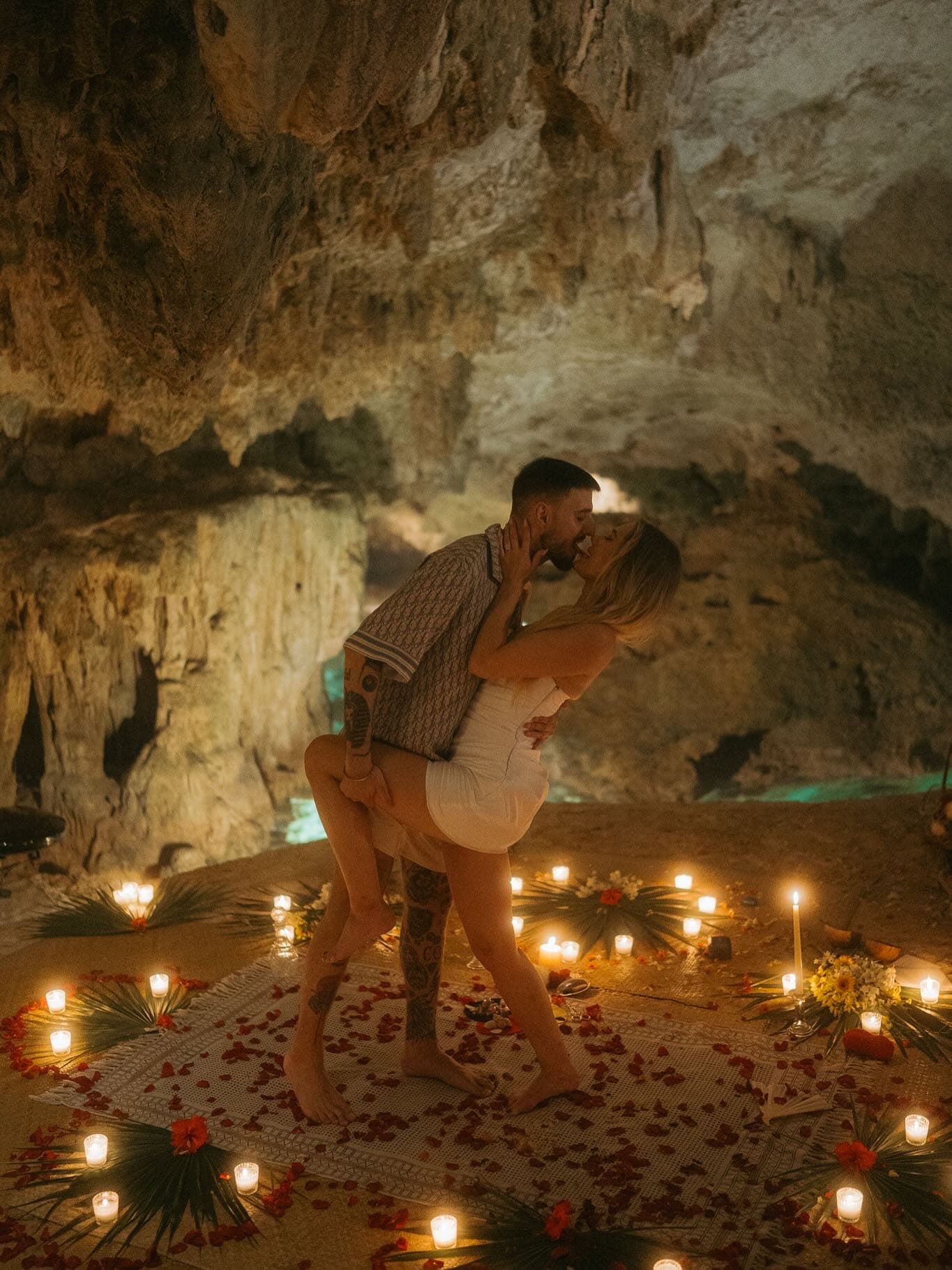 A couple embracing on a mandala of candles and rose petals laid across the cave floor