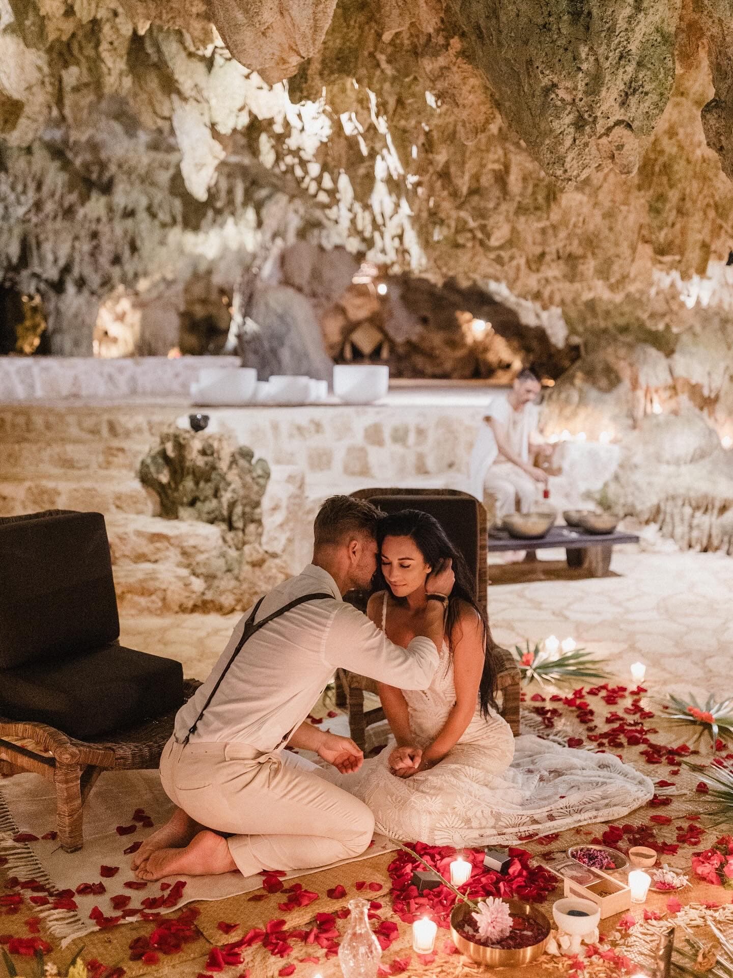 A couple seated together among candles and petals, the lit cave behind them