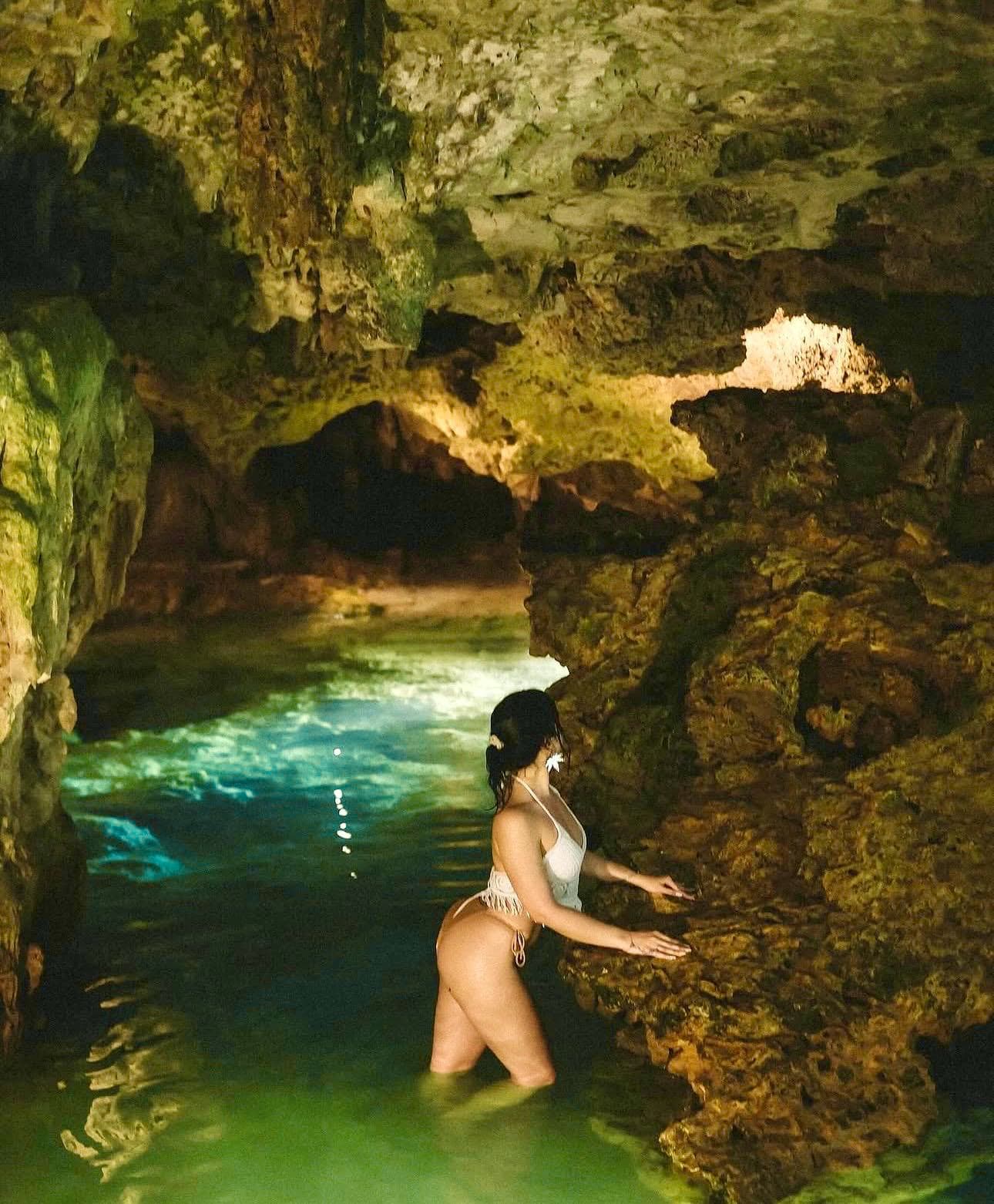 A guest reaching out across the turquoise water, the cave arching over her