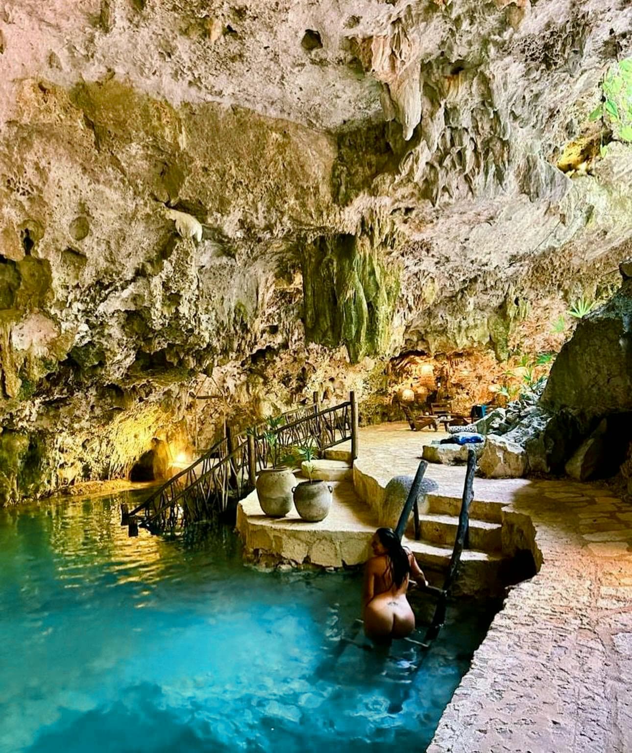 A guest on the wooden ladder at the edge of the cenote, the lantern-lit walkway behind her