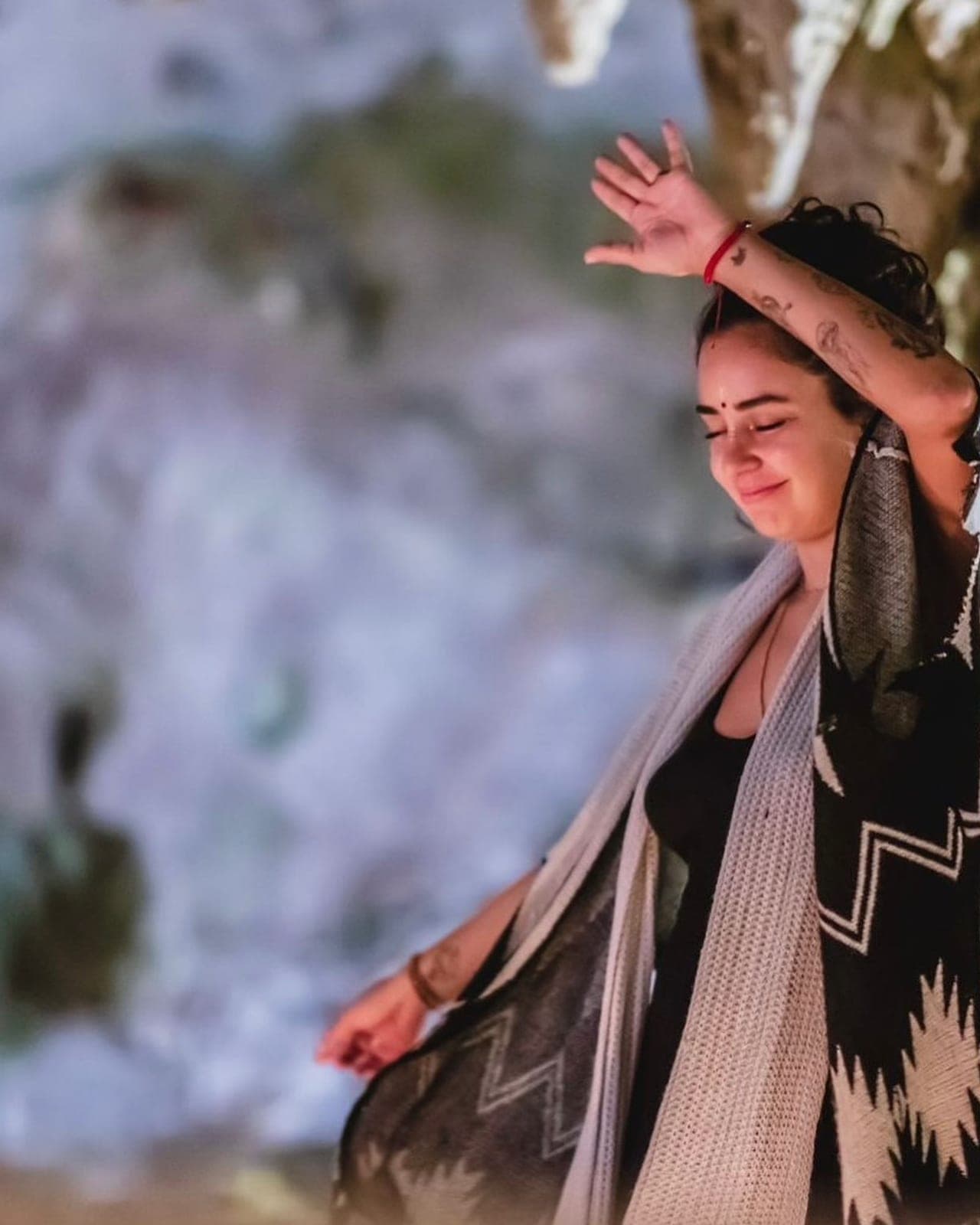 Una huésped bailando con los ojos cerrados y los brazos en alto, envuelta en un chal estampado contra el muro de la cueva