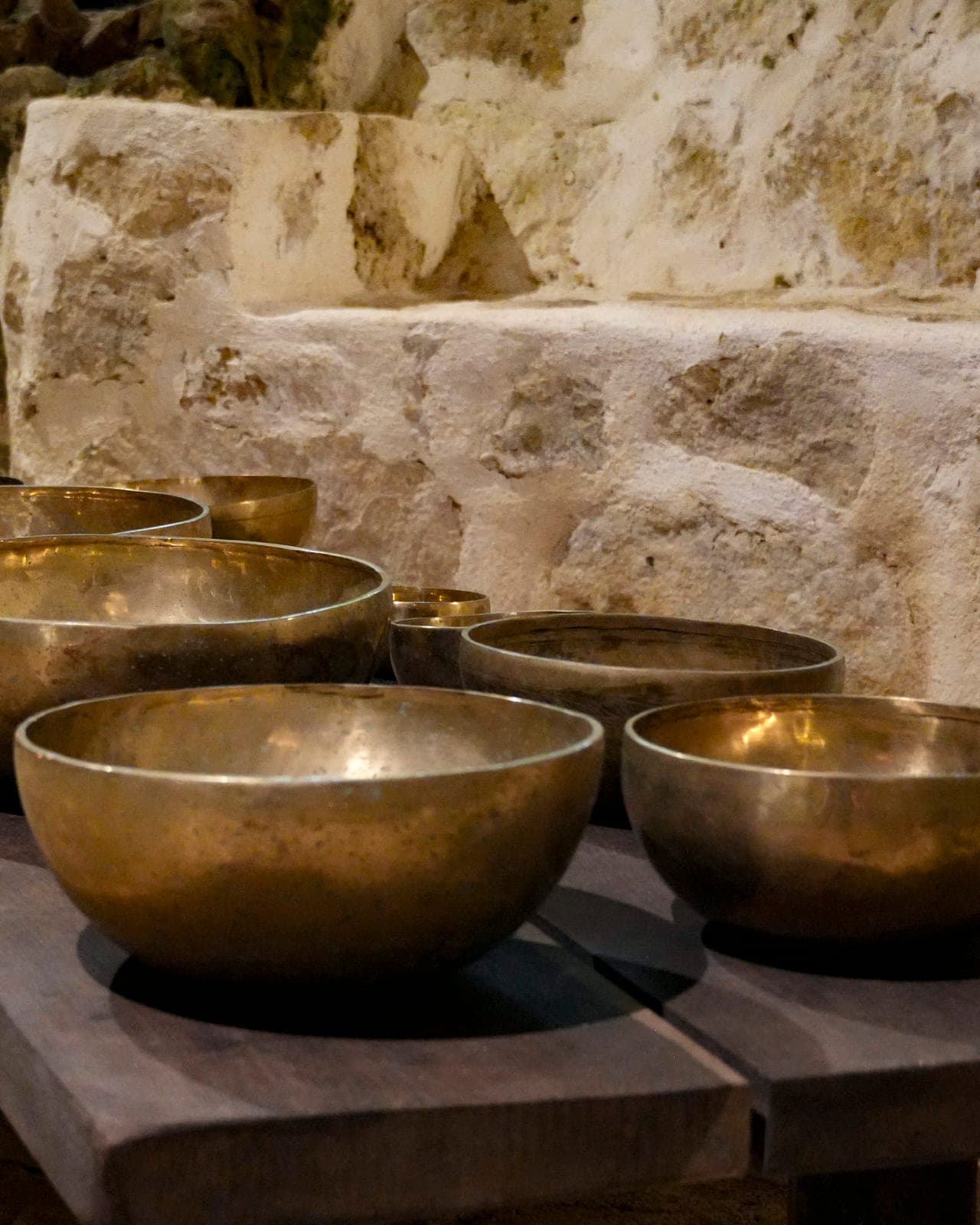 Una hilera de cuencos de bronce antiguo sobre una banca de madera oscura en lo profundo de la cueva iluminada con velas