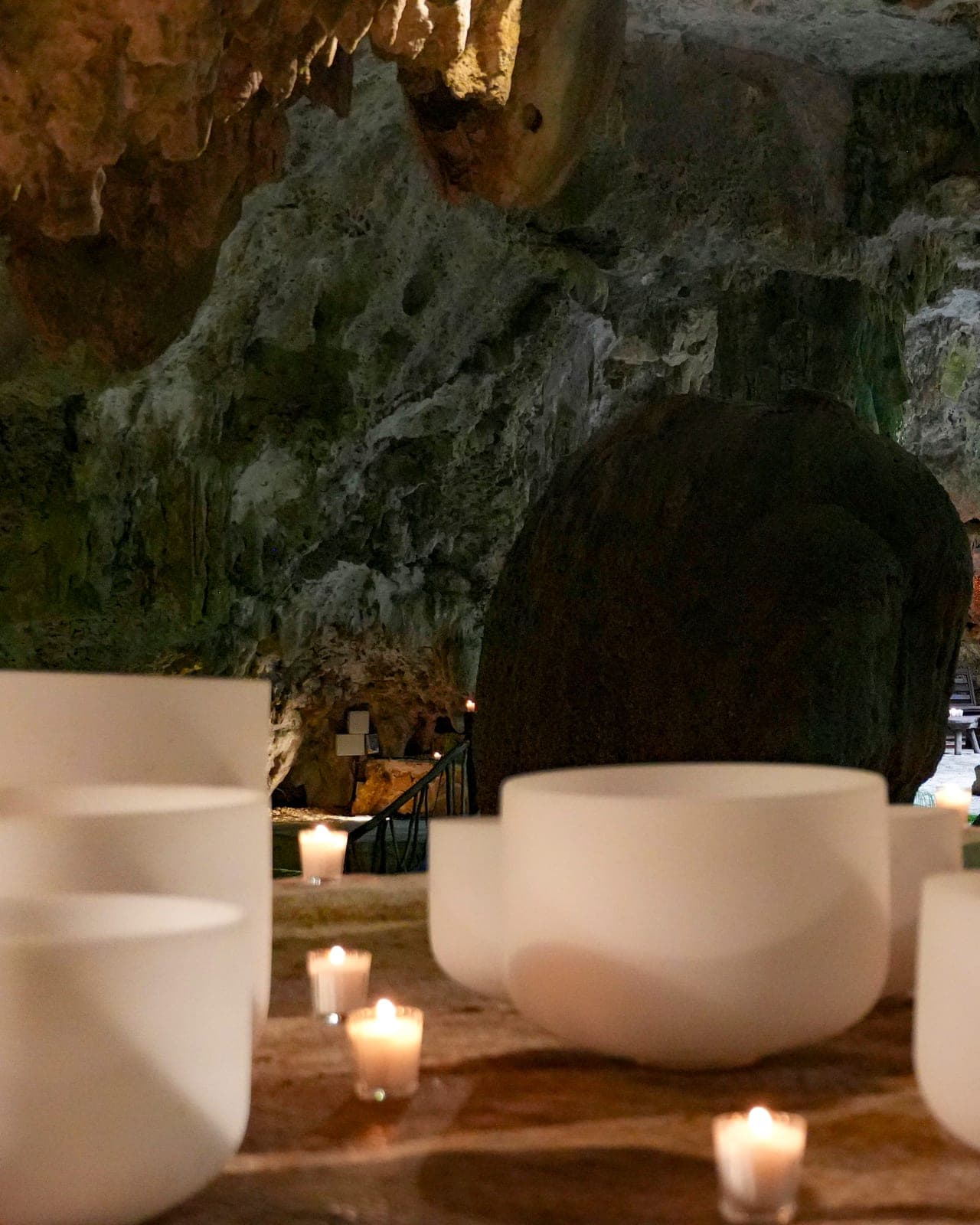 Cuencos de cristal esmerilado y veladoras encendidas sobre una banca de piedra, la luz del día entrando por la abertura de la cueva