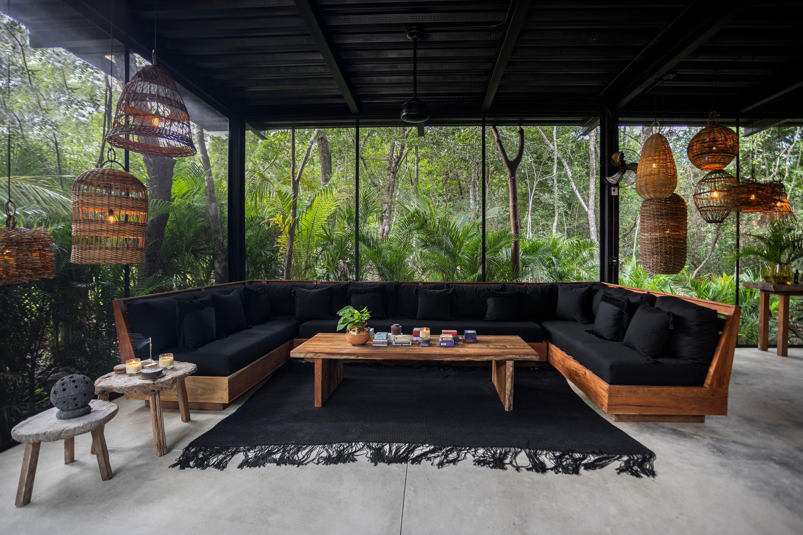 La Recepción: the long black sofa around the low wooden table, jungle on every side through the glass