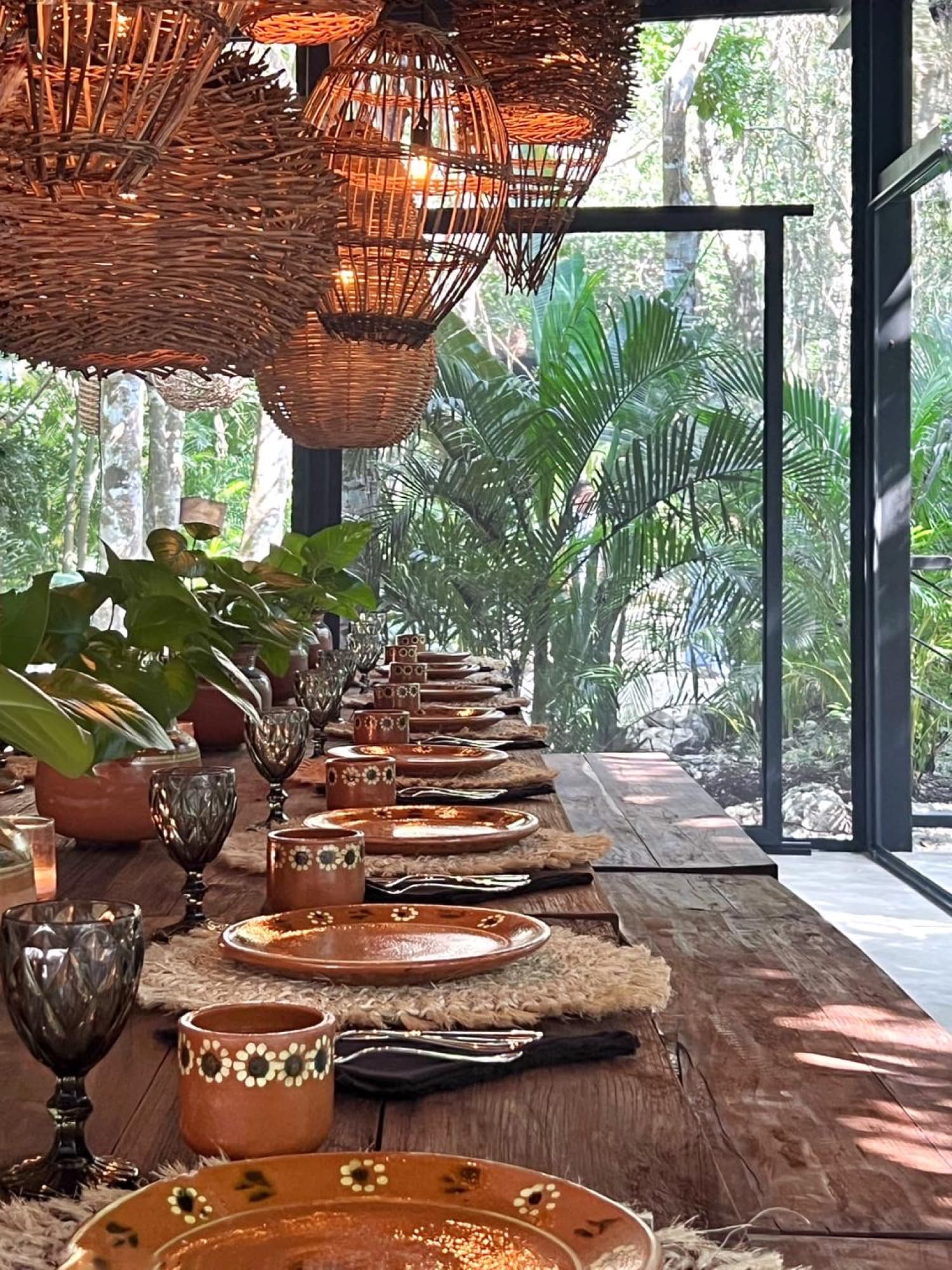 Down the length of the table: clay plates on woven mats, palms beyond the glass