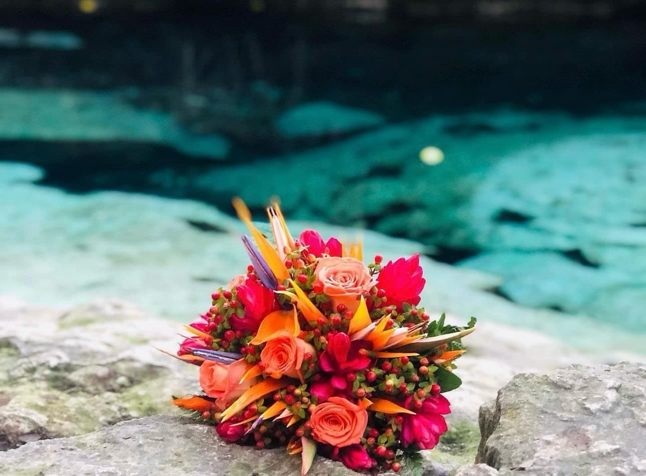 A bouquet of roses and birds of paradise resting on the rock beside the turquoise cenote