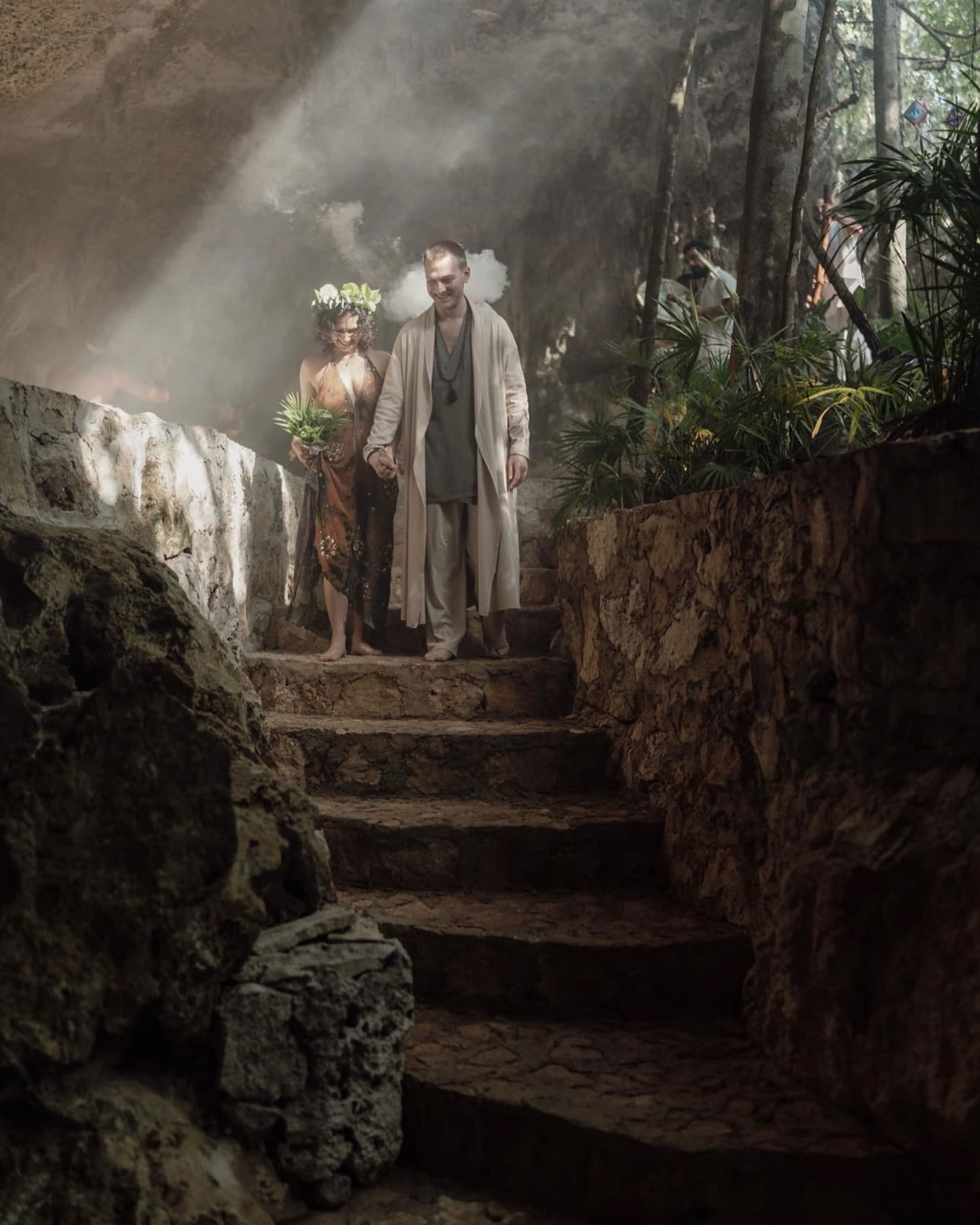 A couple on the cave stair in a shaft of daylight, the jungle above the opening