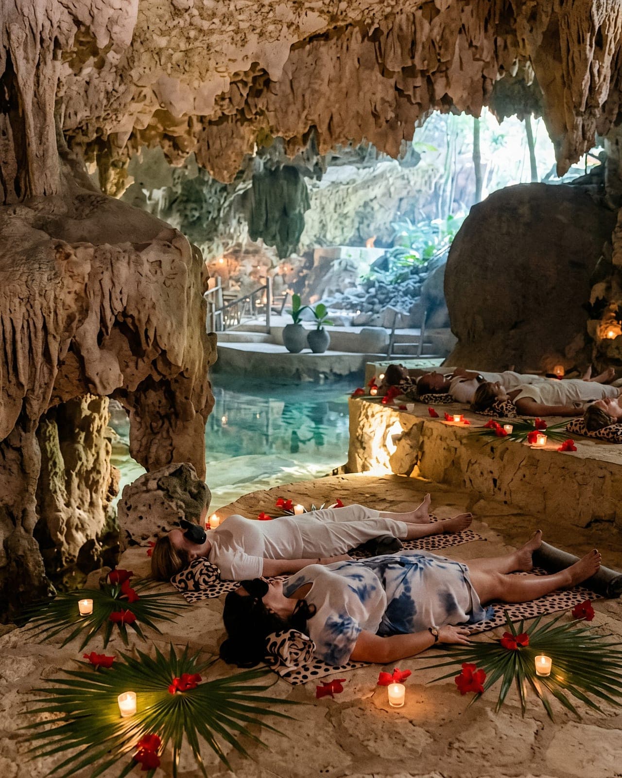 Guests lying on the limestone terraces in eye masks, among candles and palm fronds, the cenote opening behind them