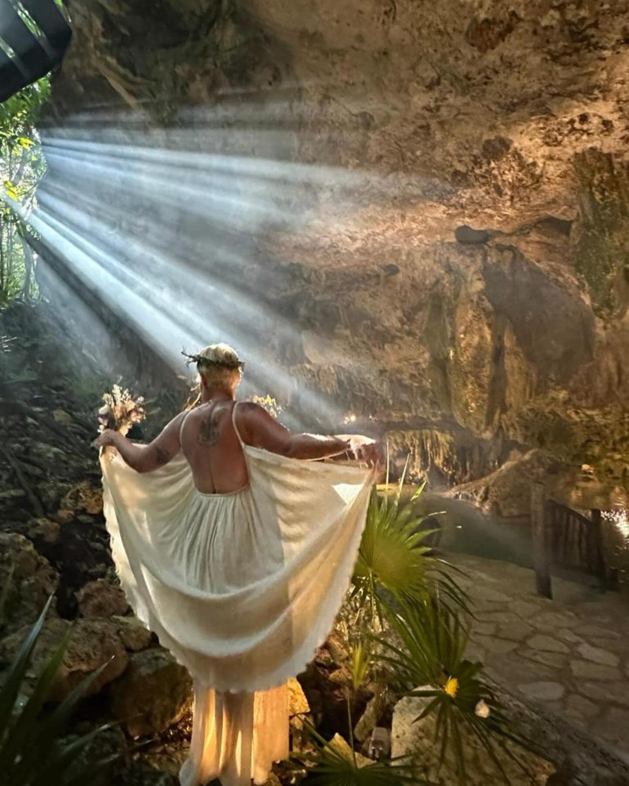 A woman in a white dress opening its skirt like wings in the shaft of daylight at the mouth of the cave