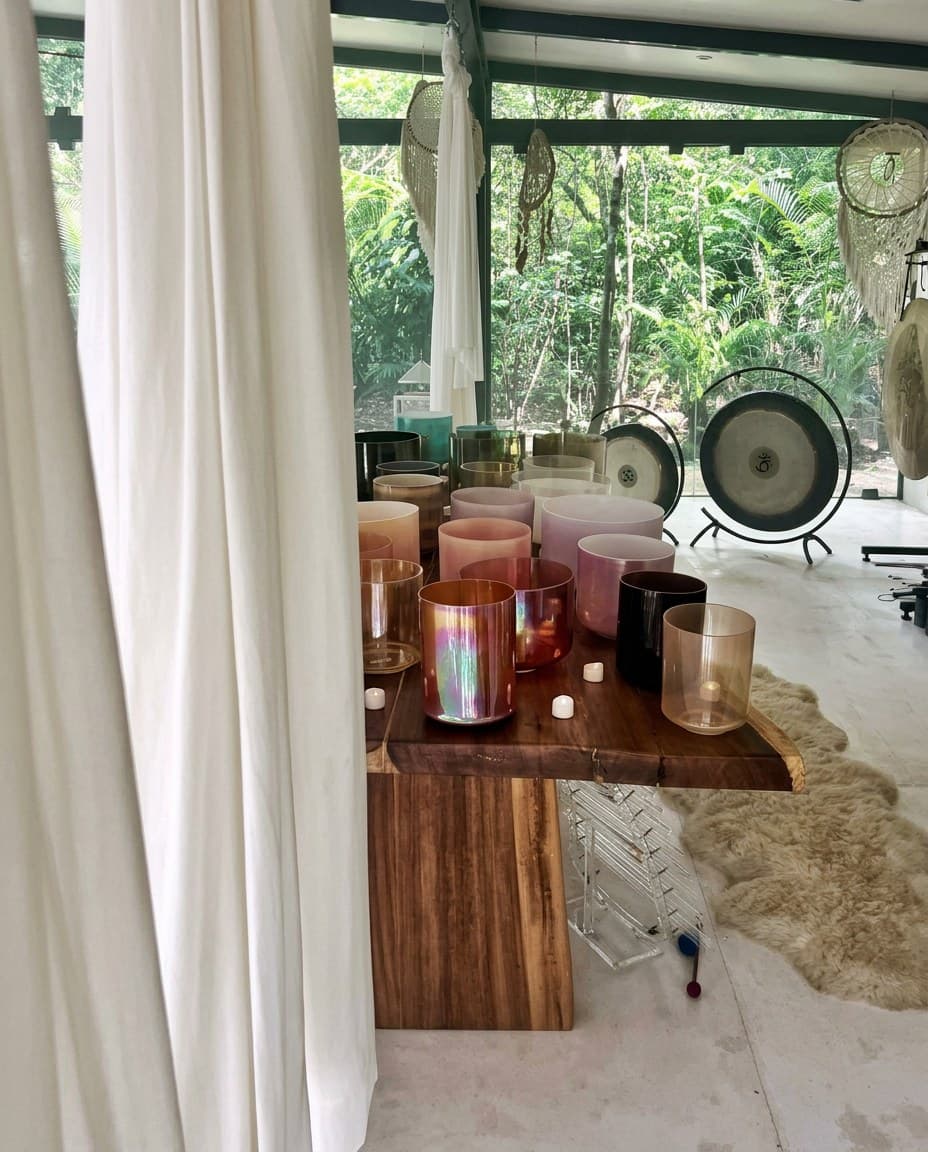 El altar de cuencos de cristal sobre la mesa de madera viva en el templo de cristal, sedas blancas cayendo a un lado y los gongs planetarios contra la selva