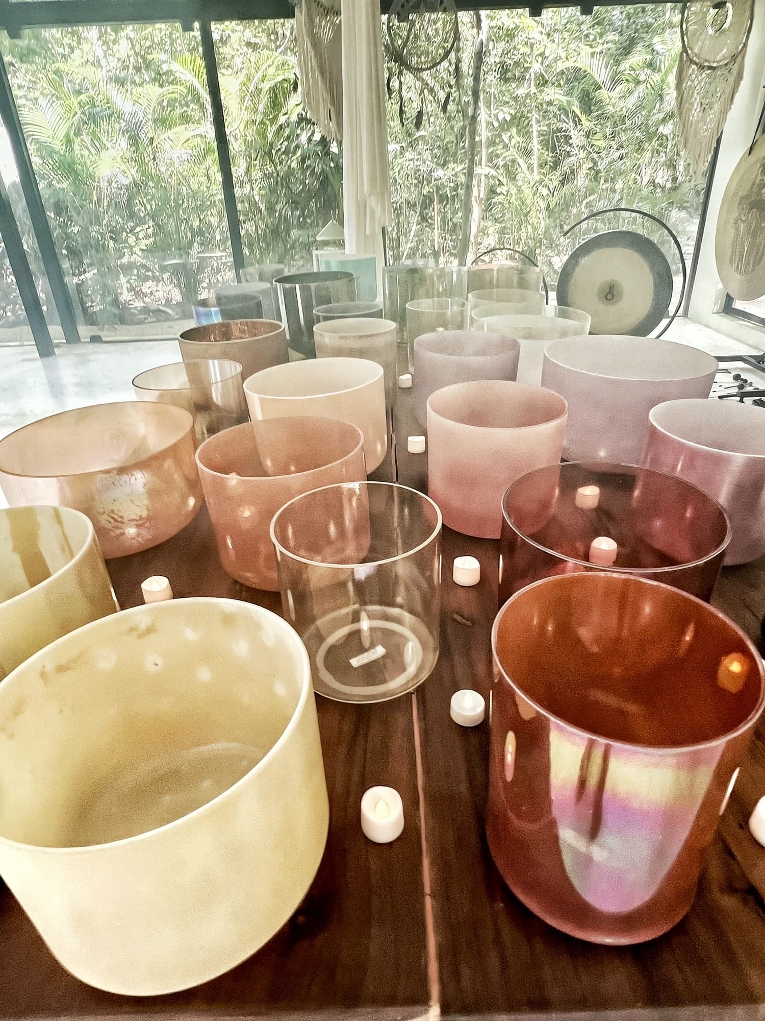 Alchemy crystal singing bowls in rose, amber and clear quartz ranged across the wooden table of the Sound Temple, a planetary gong behind