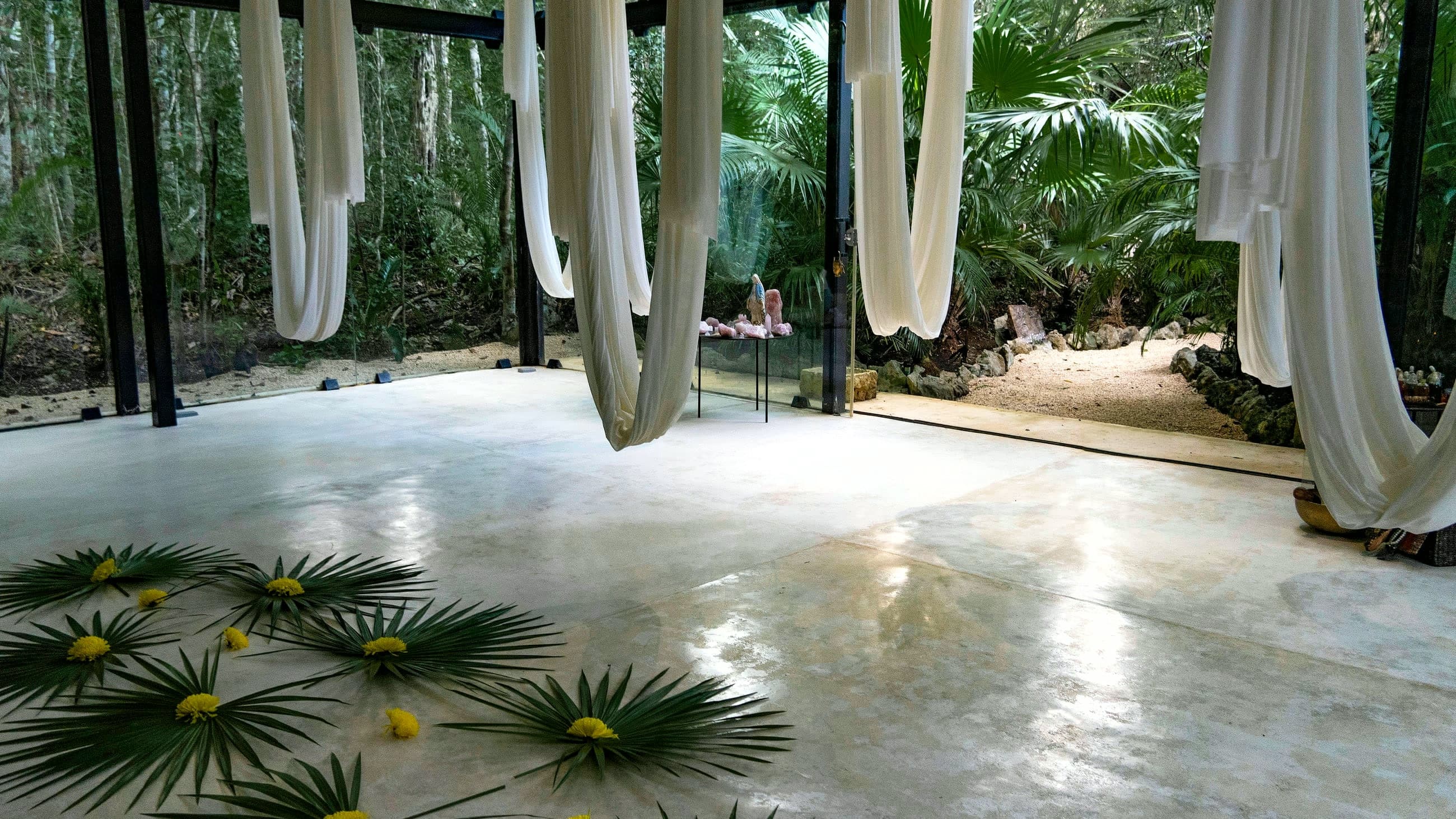 The empty Sound Temple: white silk hammocks hanging over the polished floor, palm fans and yellow flowers laid out, the jungle through the glass