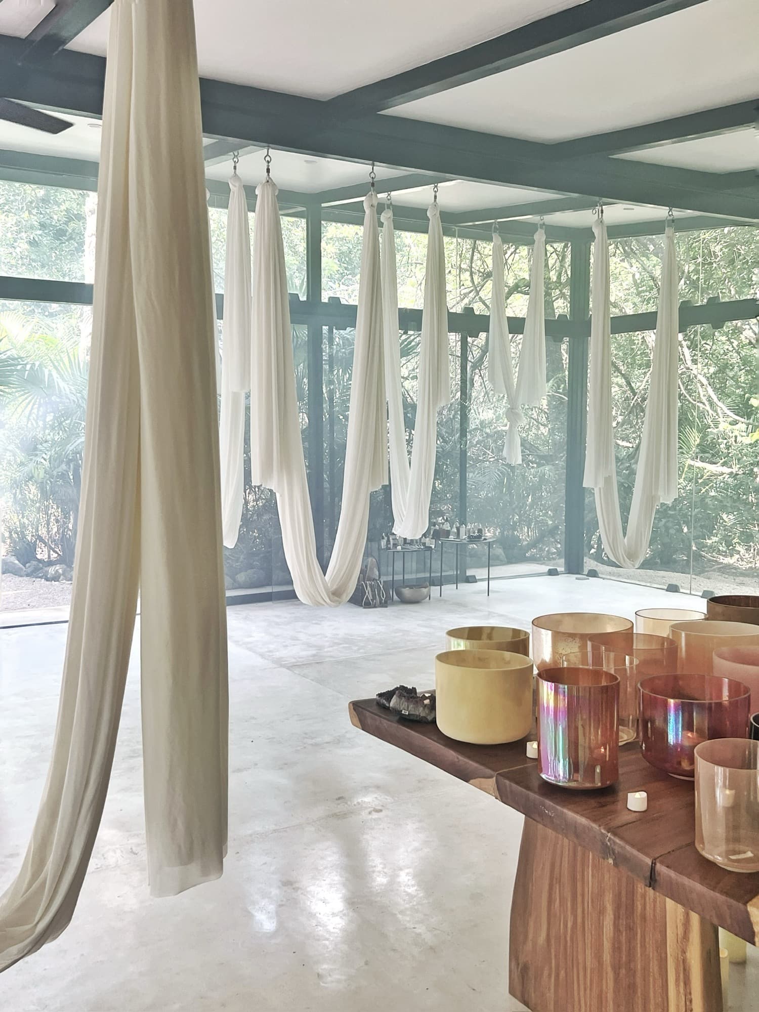 Silk hammocks hanging the length of the Sound Temple in daylight, the crystal bowls on the wooden altar and the jungle green through every pane