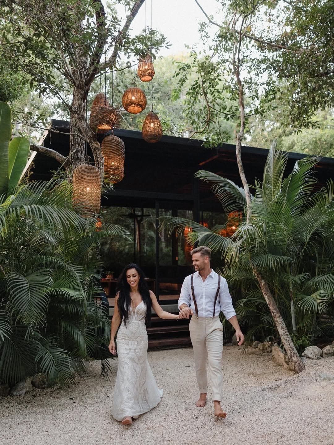 A bride and groom walking out hand in hand beneath the woven lanterns